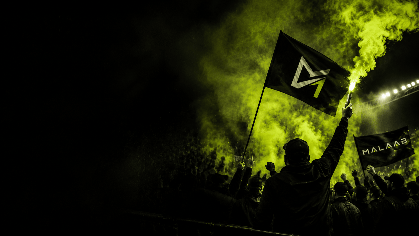 Malaab supporters lighting a flare with the brand flag and banner